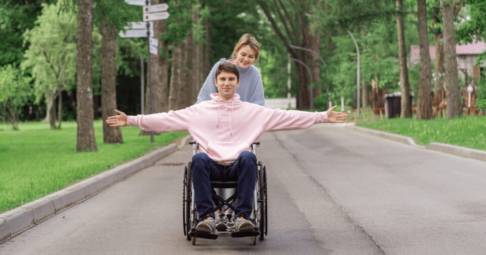 Pildil on noormees ratastoolis. Ratastooli taga seisab noor neiu.